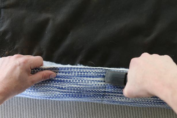 With the help of a friend, stretch the rug across the batting and onto the back of the cushion support. Once itâs taut, secure the stretched rug in place using a staple gun and staples. TIP: If youâre recovering a boxed cushion ottoman, you will also need to attach side panels to the top panel using a round-ended tapestry needle and a 2-ounce skein of mercerized cotton in a coordinating color.