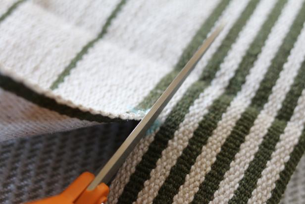 Use dressmaker shears to cut the third flat weave rug into four side panels for the slipcover. Two will be cut to the length of the pet bed and two will be cut to the width of the pet bed.