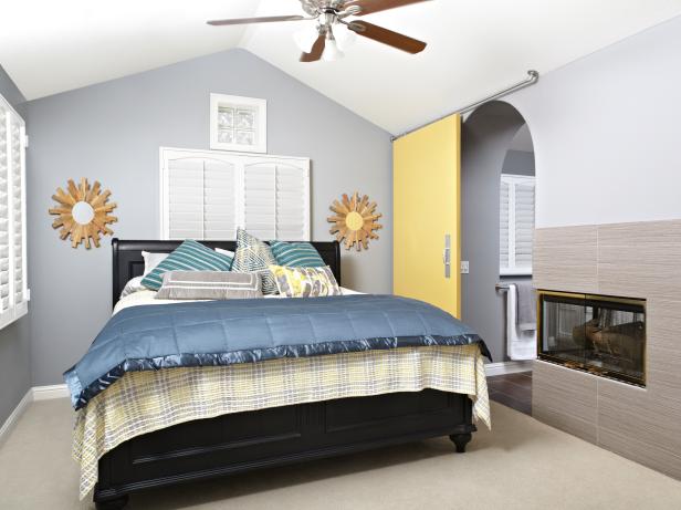 A comfortable and cheery bedroom in neutral tones offers plantation shutters and a wall fireplace which it shares with the bathroom. A yellow sliding barn door and arched doorway are unique features of this bedroom.