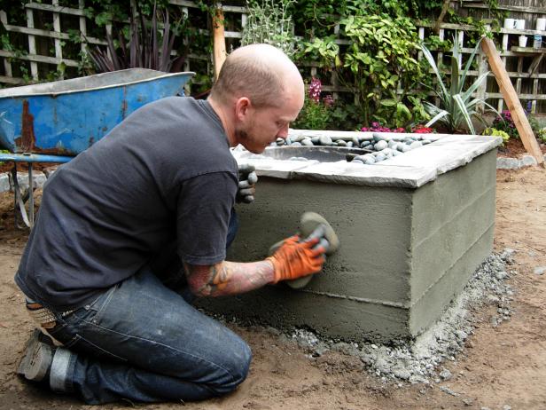 With a sweet design and hard work, this backyard comes to life with a concrete chic fire feature. Contractor smooths out concrete mortar on sides of fire feature exterior using sponge. Rocks and bowl sit inside the interior of the project.