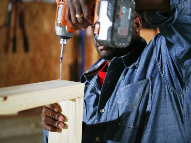 Man uses a drill to attach the wood pieces of the doghouse frame.