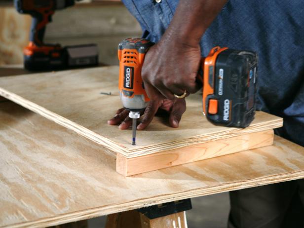 Constructing a dog house, while attaching the wood pieces together using a drill.