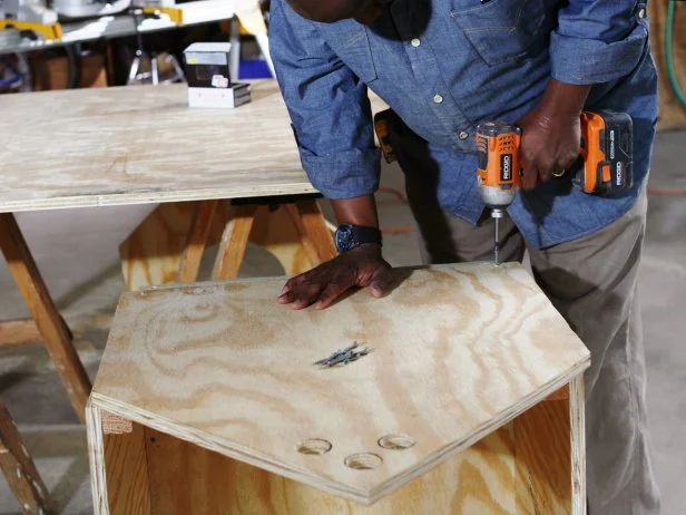 Man uses a drill to attach the back panel of the doghouse frame.