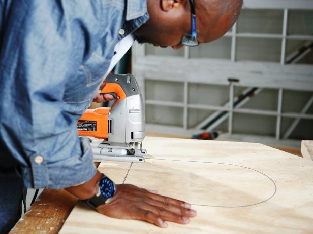 Man uses a saw to cut out traced area on plywood.