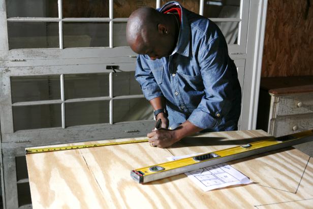 African american man draws next to a measuring top on a piece of wood to construct a doghouse.