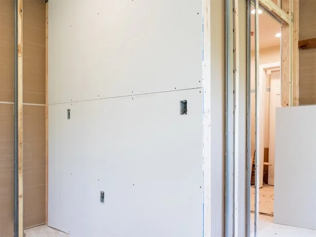 Attach lower wallboard to studs, making sure drywall fits snugly over outlets and switches.
