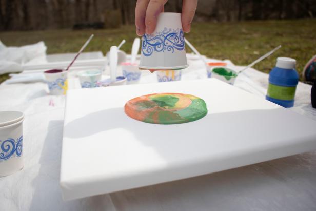 Have your child lift the cup slowly so that the paint begins to flow out across the canvas. As opposed to a spilling pour, the paint is guaranteed to start in the center of the canvas and expand in all directions.