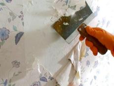 Closeup of person using a scraper to remove old wallpaper from wall. 