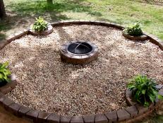 A fire pit made with stones as well as a fire pit area surrounding it with gravel. Plants were added as well.